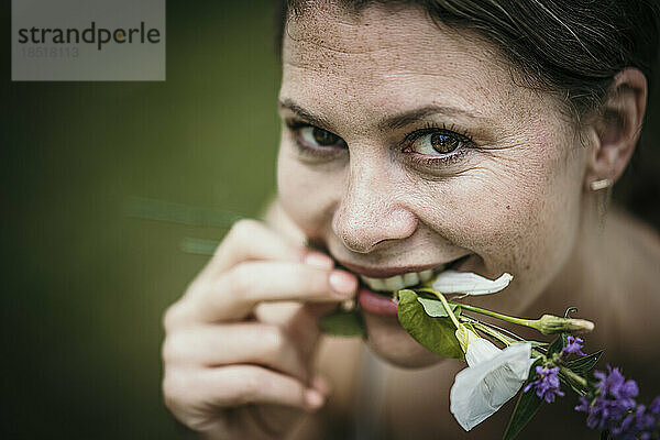 Smiling woman holding flowers in mouth