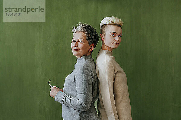 Selbstbewusste Frauen mit kurzen Haaren stehen an einer grünen Wand