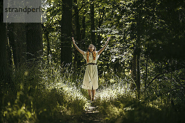 Frau mit erhobenen Armen steht im Wald