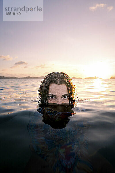 Frau versteckt Gesicht im Wasser am Strand bei Sonnenuntergang