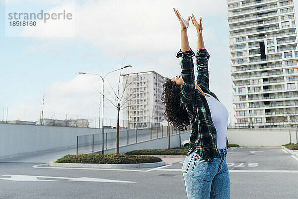 Sorglose junge Frau tanzt mit erhobenen Armen auf dem Parkplatz