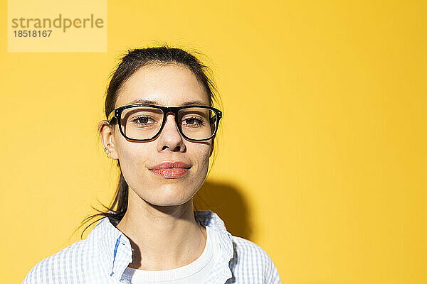 Lächelnde junge Frau mit Brille vor gelbem Hintergrund