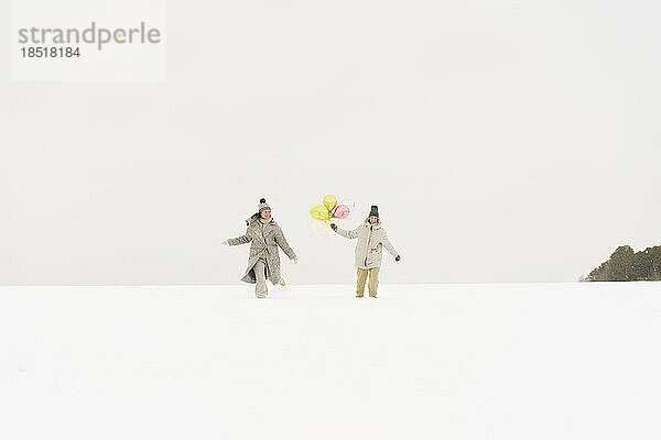 Freunde gehen mit Ballon im Schnee spazieren