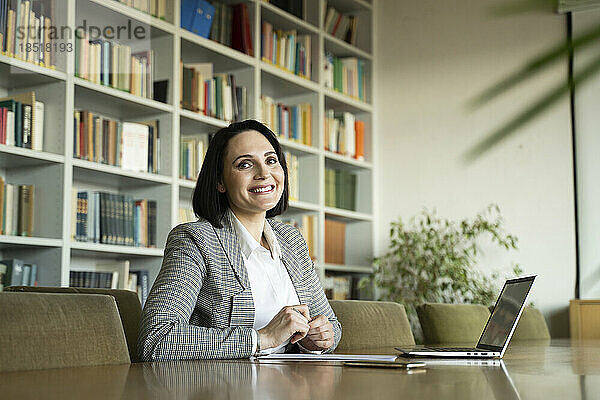 Glückliche Geschäftsfrau mit Laptop sitzt am Schreibtisch im Büro