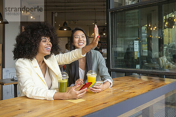 Happy woman waving by friend sitting in cafe