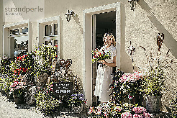 Reife Frau mit Blumen steht am Eingang eines Blumenladens