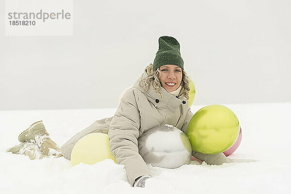 Glückliche Frau mit Luftballons und Strickmütze genießt den Schnee