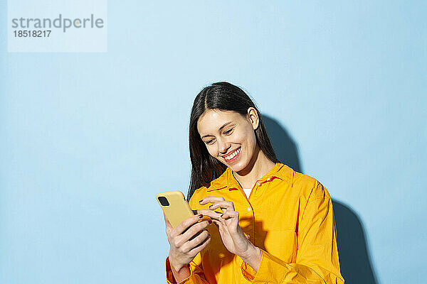 Glückliche junge Frau  die SMS mit dem Smartphone vor blauem Hintergrund sendet