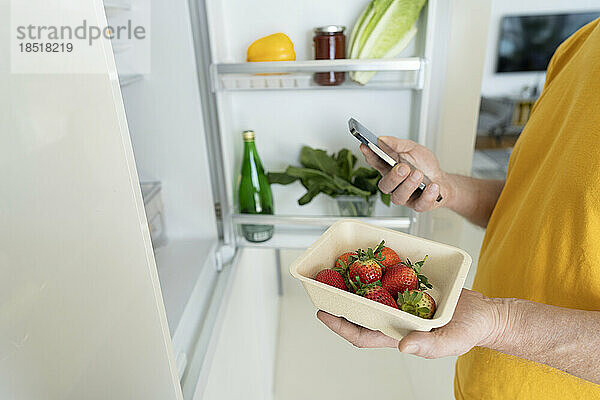 Älterer Mann hält frische Erdbeeren und Smartphone zu Hause