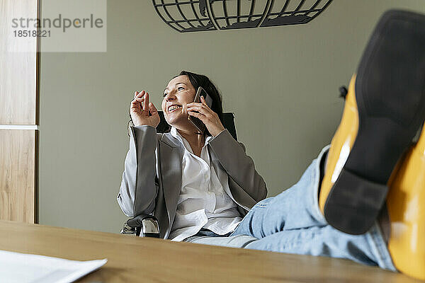 Glückliche Geschäftsfrau  die im Büro am Smartphone spricht