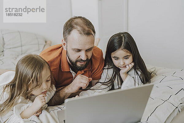 Vater und Töchter schauen auf den Laptop im Bett