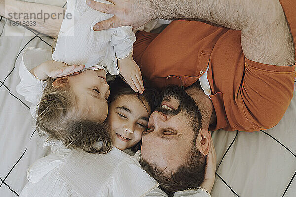 Happy father embracing daughters on bed at home