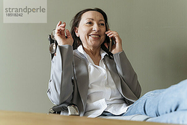 Glückliche Geschäftsfrau  die im Büro am Handy spricht