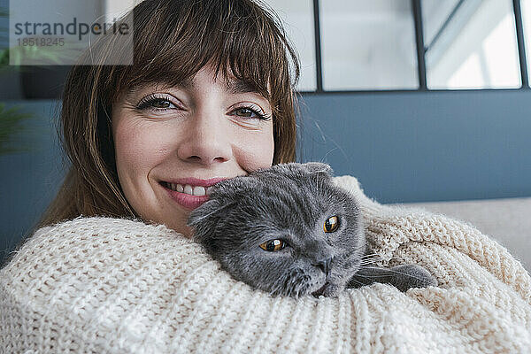 Lächelnde Frau umarmt Katze zu Hause