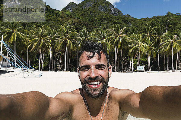 Glücklicher Mann  der am Strand ein Selfie macht