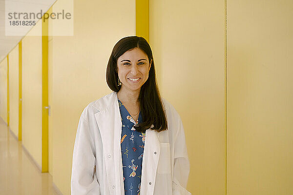 Lächelnder Arzt im Laborkittel steht neben gelber Wand