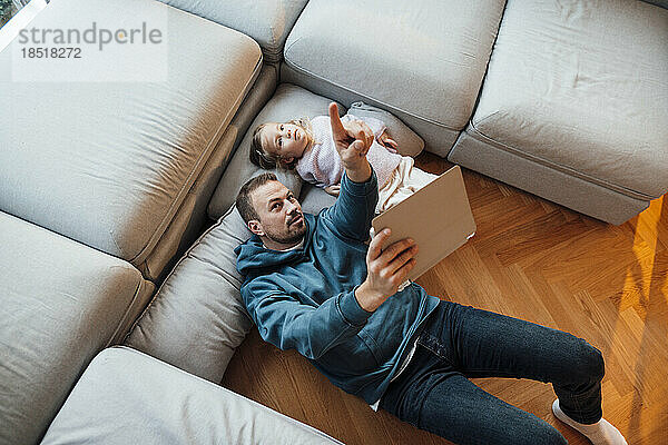 Vater hält Tablet-PC in der Hand und gestikuliert mit Tochter  die zu Hause liegt