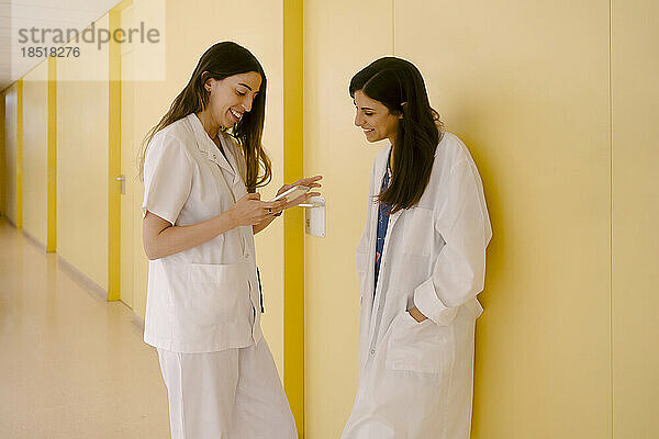 Lächelnde Ärzte teilen sich ihr Smartphone im Flur