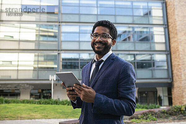 Lächelnder Geschäftsmann mit Tablet-PC vor Bürogebäude