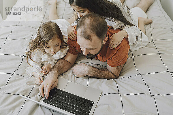 Töchter mit Vater benutzen Laptop zu Hause im Bett