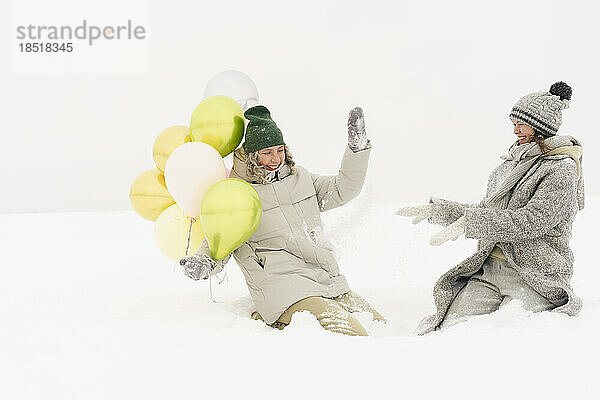 Fröhliche Freunde  die Spaß mit Luftballons im Schnee haben