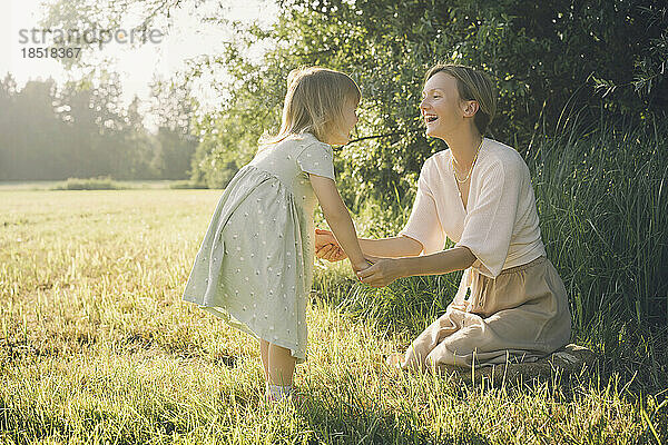 Glückliche Mutter hält Händchen mit ihrer Tochter an einem sonnigen Tag in der Natur
