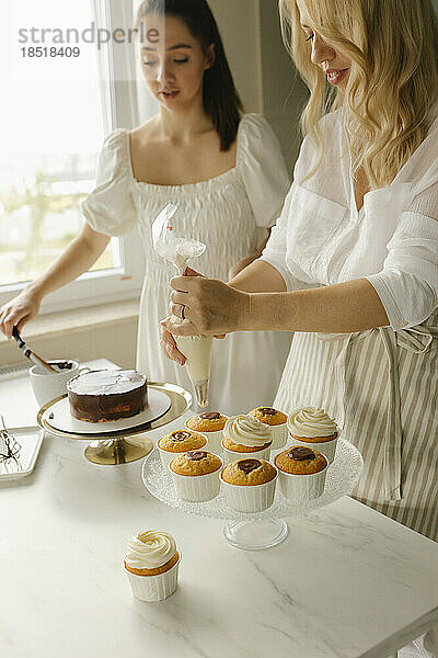 Frau mit Freundin bereitet zu Hause Kuchen zu und dekoriert Cupcakes