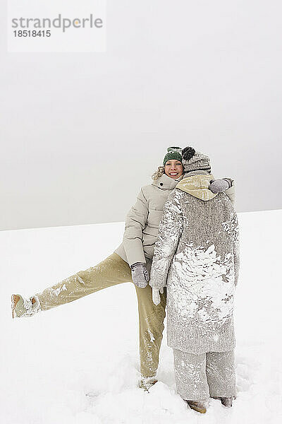 Happy woman standing on one leg embracing friend in snow
