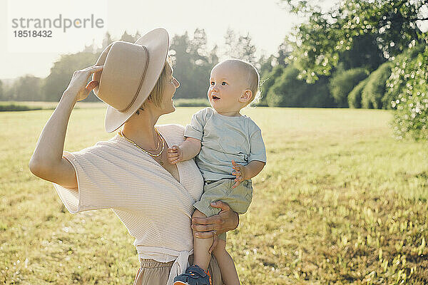 Happy mother wearing hat and carrying son in nature