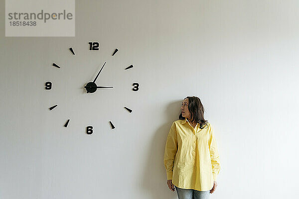 Frau blickt auf große Uhr an weißer Wand