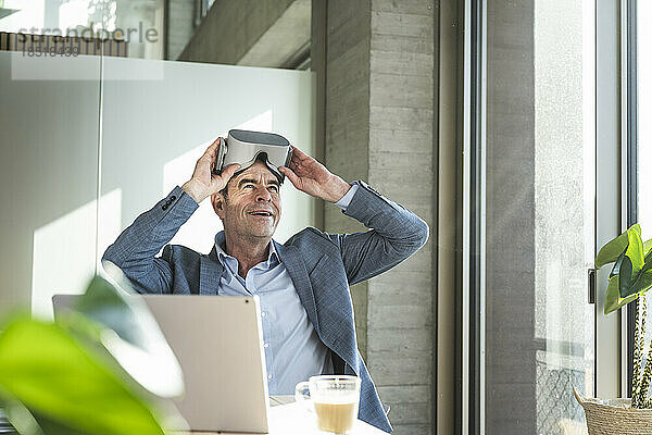 Reifer Geschäftsmann mit Virtual-Reality-Simulator sitzt im Büro