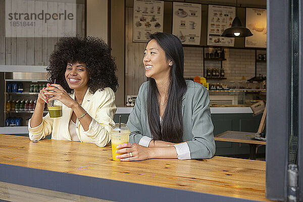 Lächelnde Frauen sitzen zusammen mit Saft am Tisch im Café