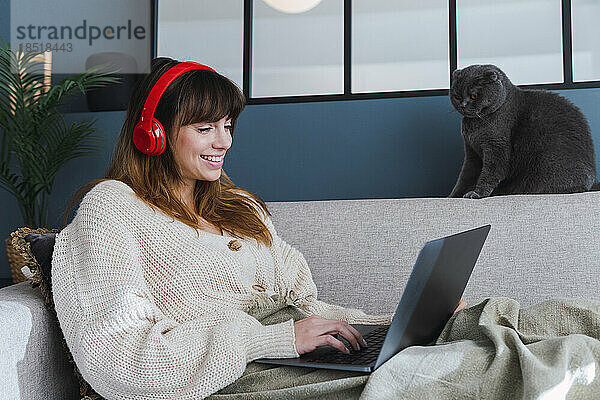 Lächelnde Frau  die zu Hause auf dem Sofa sitzt und einen Laptop benutzt