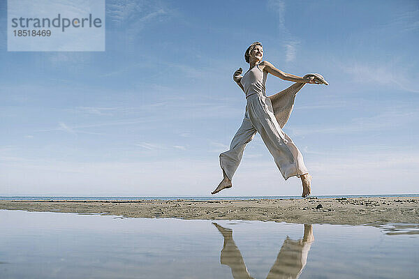 Spiegelbild einer glücklichen Frau  die am Strand springt