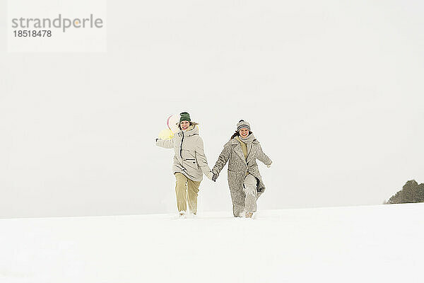 Glückliche Freunde  die Händchen haltend im Schnee spazieren gehen