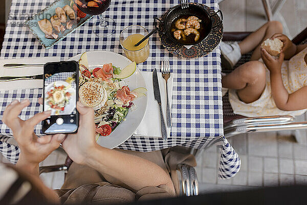 Frau fotografiert Essen mit Smartphone im Restaurant