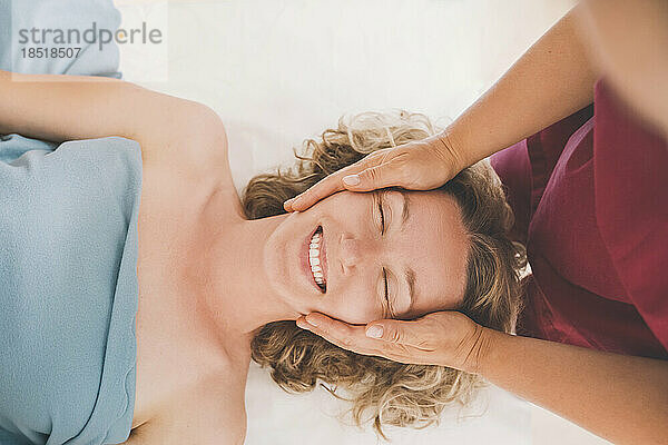 Therapist giving head massage to happy customer in salon