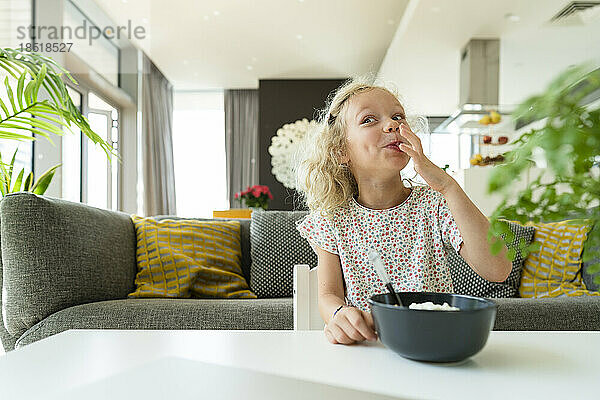 Lächelndes Mädchen genießt das Frühstück im heimischen Wohnzimmer