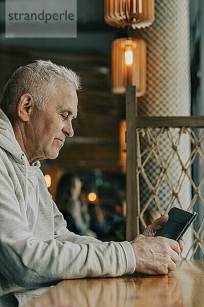 Älterer Mann sitzt im Café und benutzt Smartphone