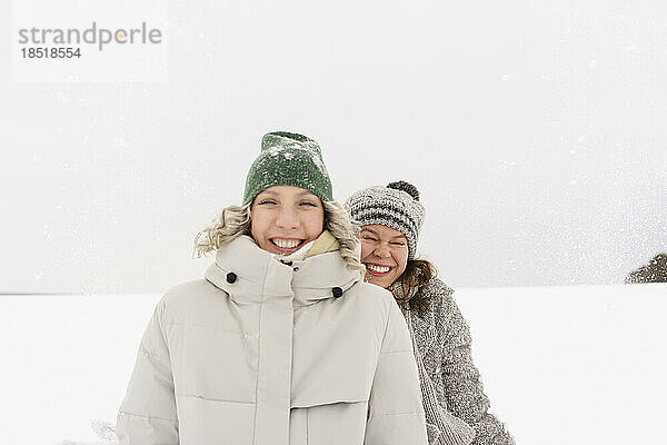 Fröhliche Freunde mit Strickmützen stehen im Schnee