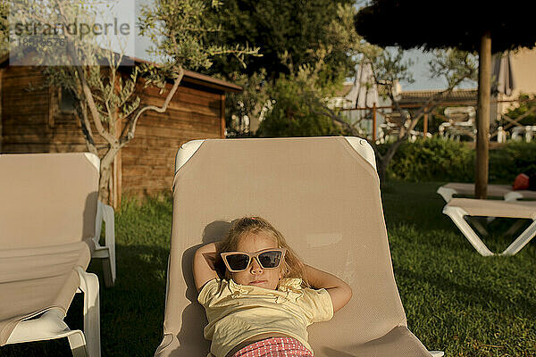 Cute girl wearing sunglasses lying on lounge chair in resort