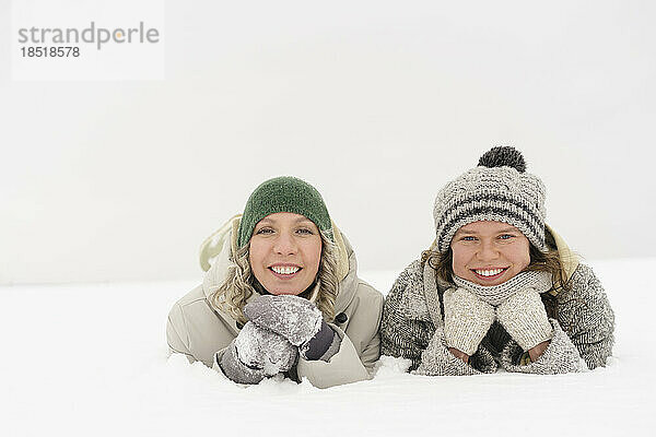 Fröhliche Freunde mit Strickmützen und Handschuhen liegen im Schnee