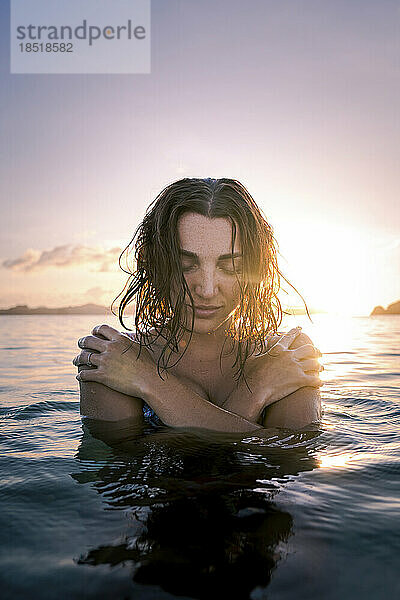 Frau mit geschlossenen Augen umarmt sich im Meer