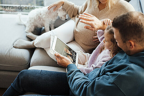 Mädchen im Videoanruf mit Großvater über Tablet-PC  der zu Hause bei den Eltern sitzt