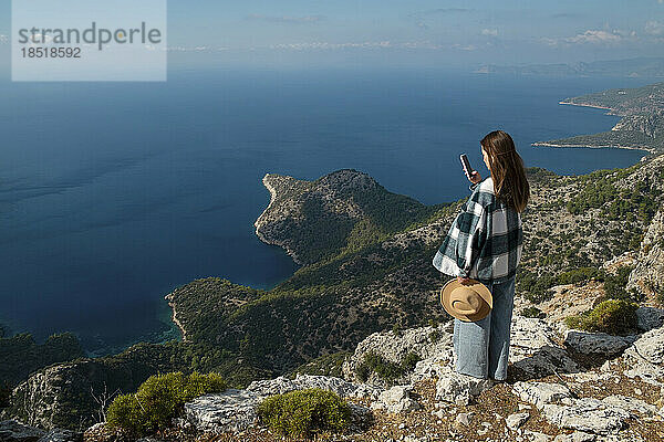 Frau fotografiert das Meer mit einem Smartphone  das auf einer Klippe steht