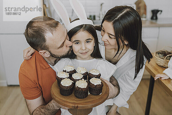 Eltern umarmen Mädchen  das zu Hause Cupcakes hält