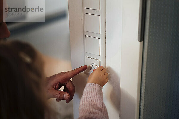 Vater hilft Tochter beim Einstellen der Temperatur am Thermostat zu Hause