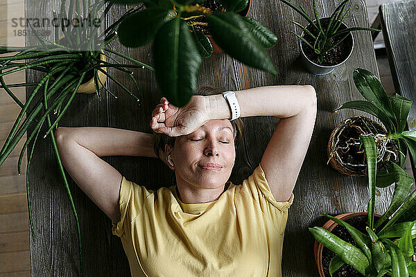 Frau mit geschlossenen Augen entspannt sich zu Hause inmitten von Pflanzen