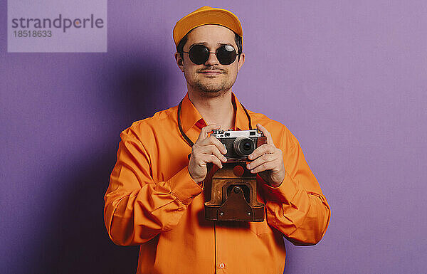 Mann steht mit Kamera im Retro-Stil vor violettem Hintergrund