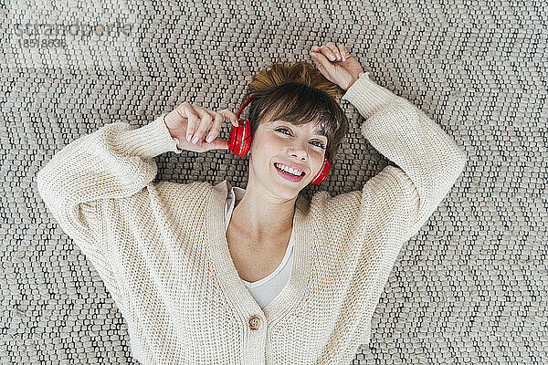 Happy woman listening music through wireless headphones lying on carpet at home